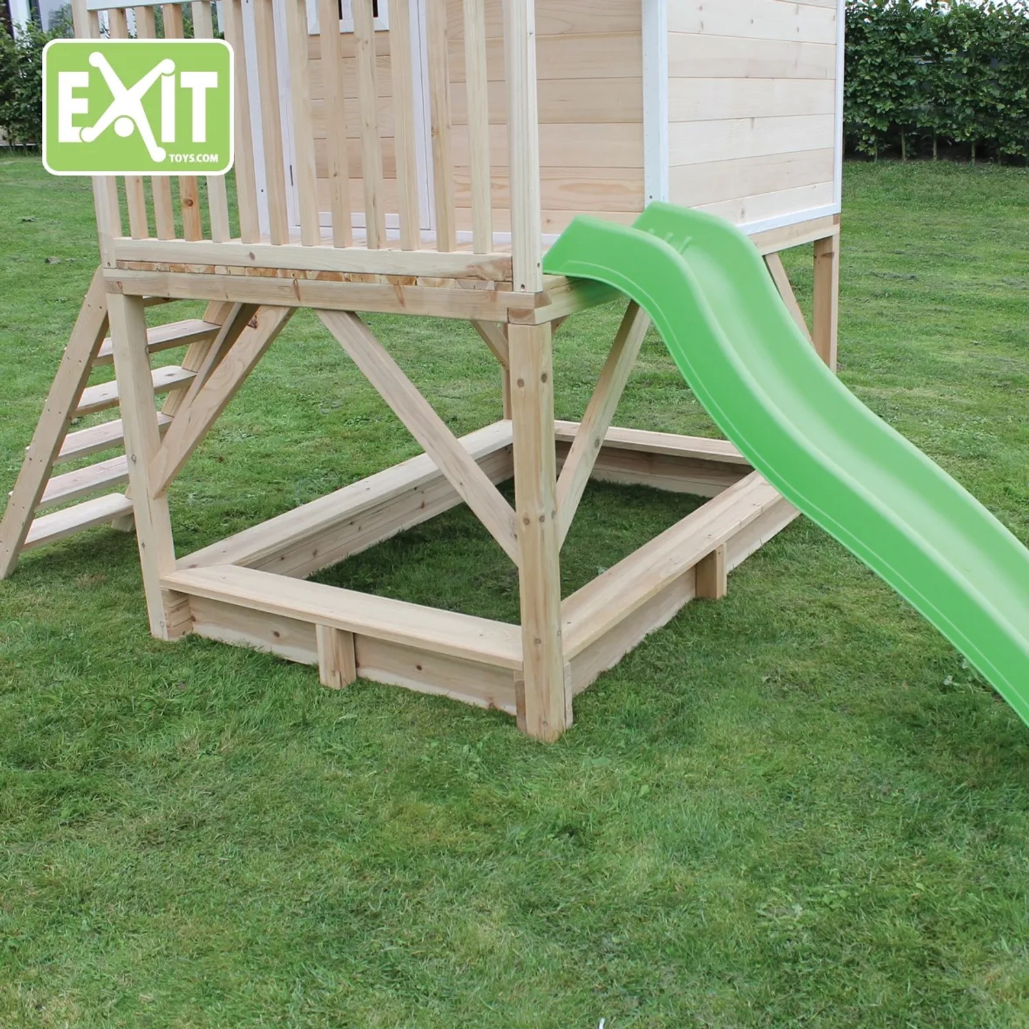 EXIT Loft 500 Holzspielhaus mit Sandkasten und grüner Rutsche im Garten.