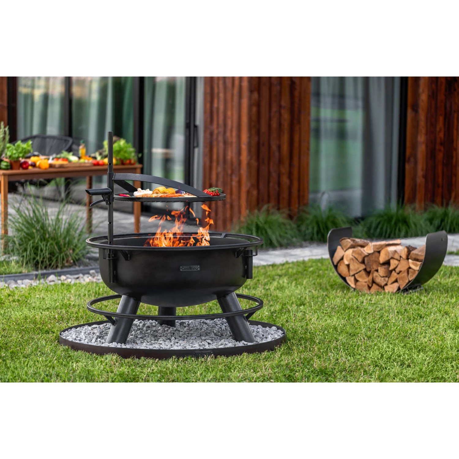 Schwarze CookKing Feuerschale Bandito mit Grillrost und Zubehör im Garten.