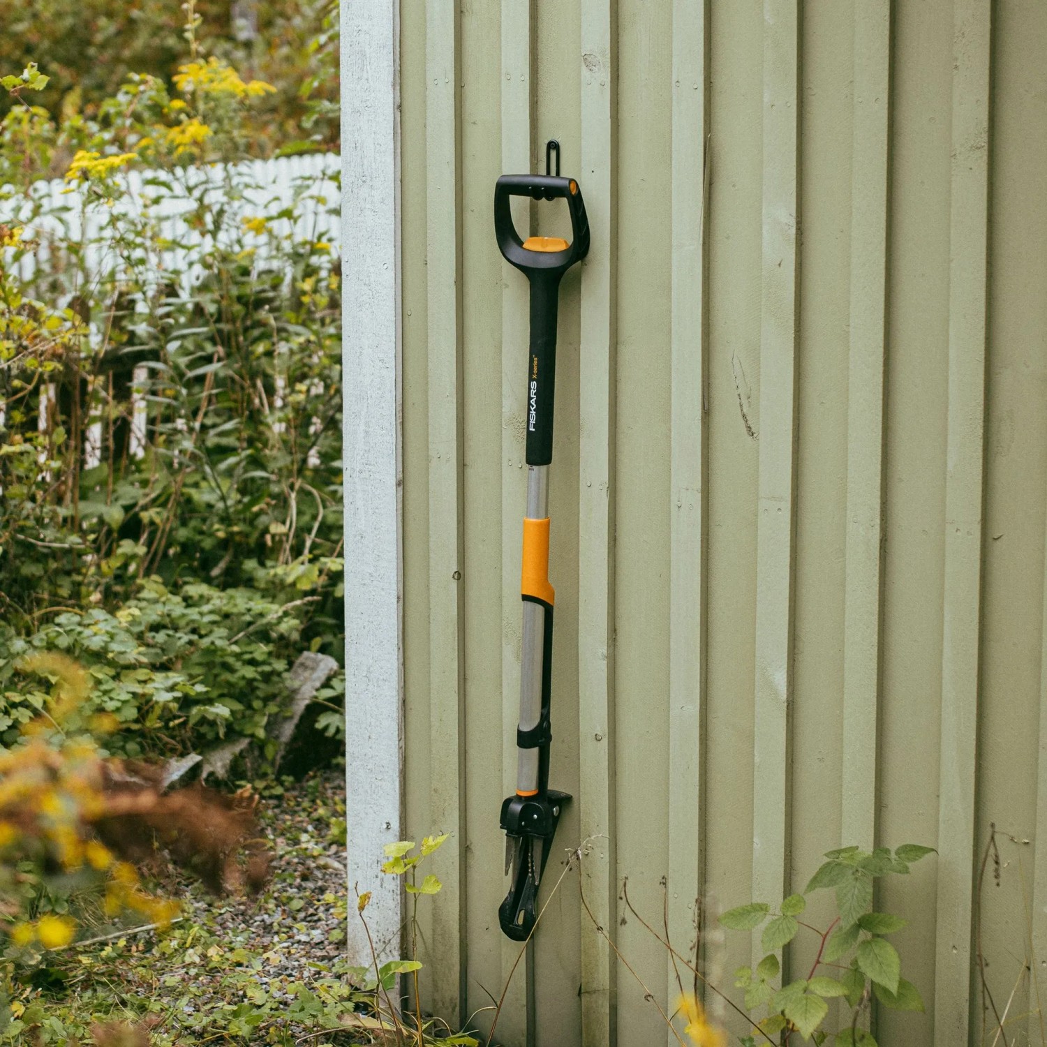 Fiskars Unkrautstecher X-Series, orange-schwarz, an einer Wand hängend.