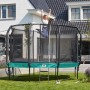 Grünes Salta Trampolin First Class (ø 366 cm) mit Sicherheitsnetz und Leiter im Garten.