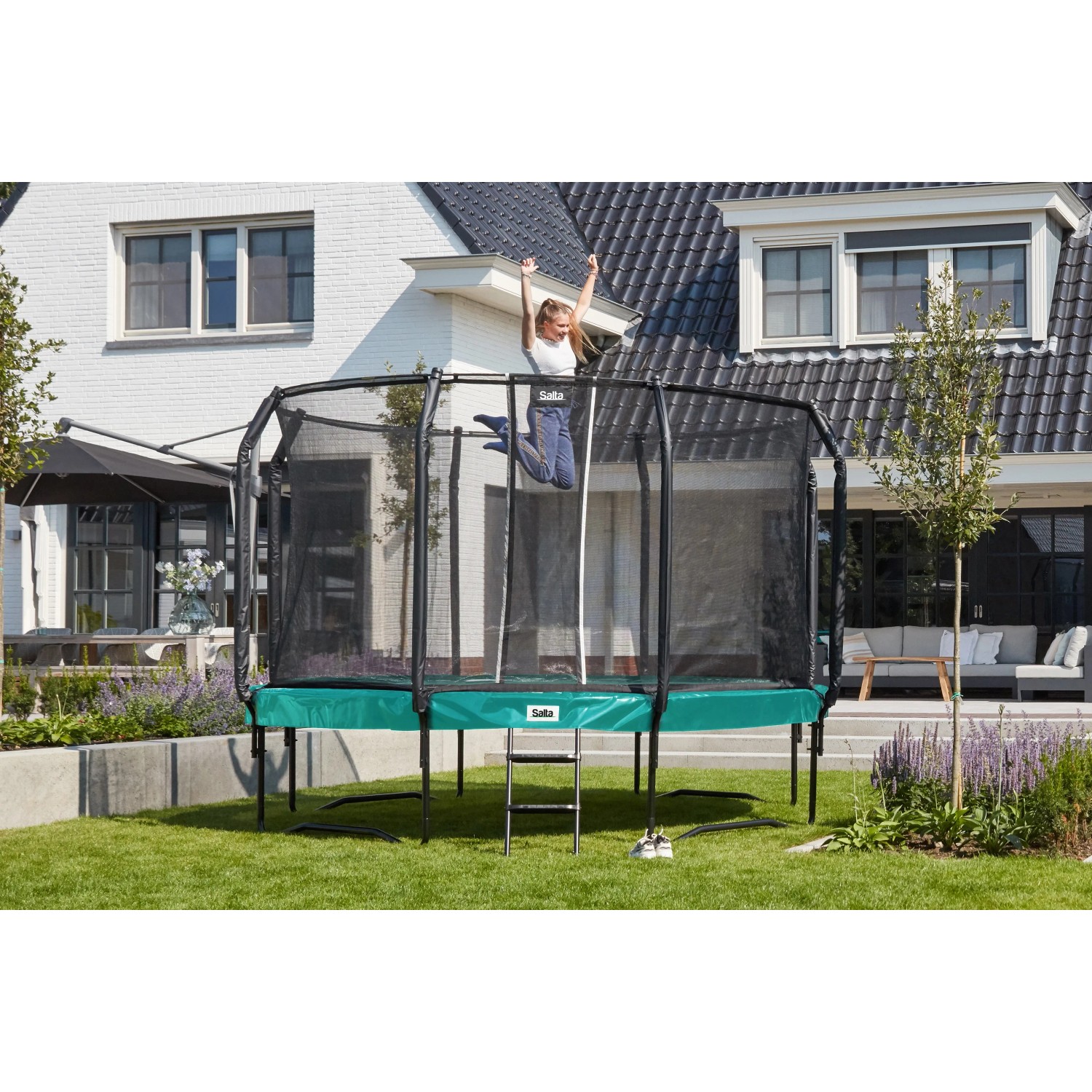 Grünes Salta Trampolin First Class (ø 366 cm) mit Sicherheitsnetz und Leiter im Garten.