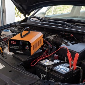 Orange Wiltec 6-12V Batterieladegerät mit LCD-Display lädt Autobatterie im Kfz-Motorraum.