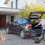 Mann saugt mit dem Bosch Akkusauger AdvancedVac 18V-8 den Kofferraum eines Autos. Hund liegt daneben.