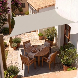Rechteckiges taupefarbenes Sonnensegel spendet Schatten über einer Terrasse mit Holzmöbeln und Pflanzen.
