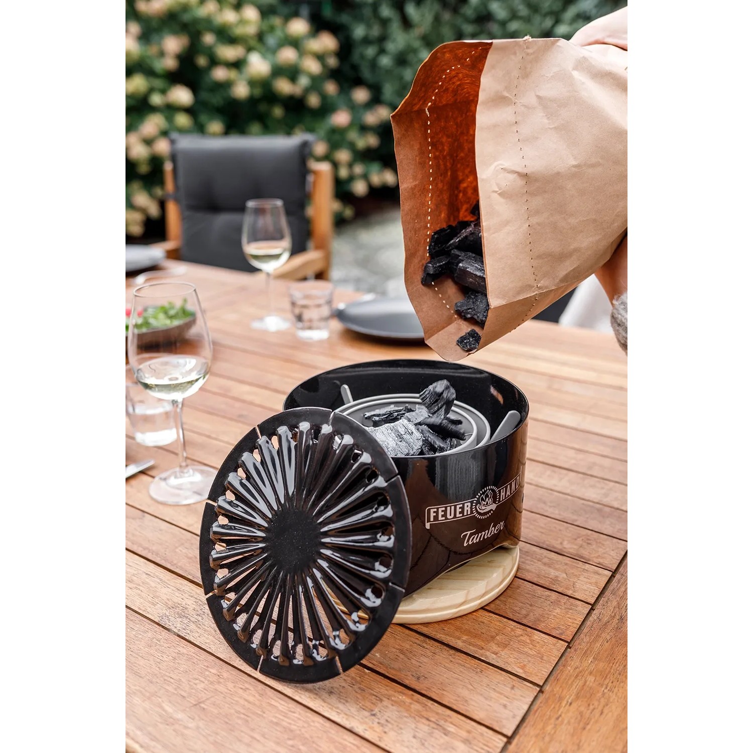 Feuerhand Tischgrill Kohle wird in Tischgrill gefüllt. Grillanzünder und Brennstoff auf Holztisch.