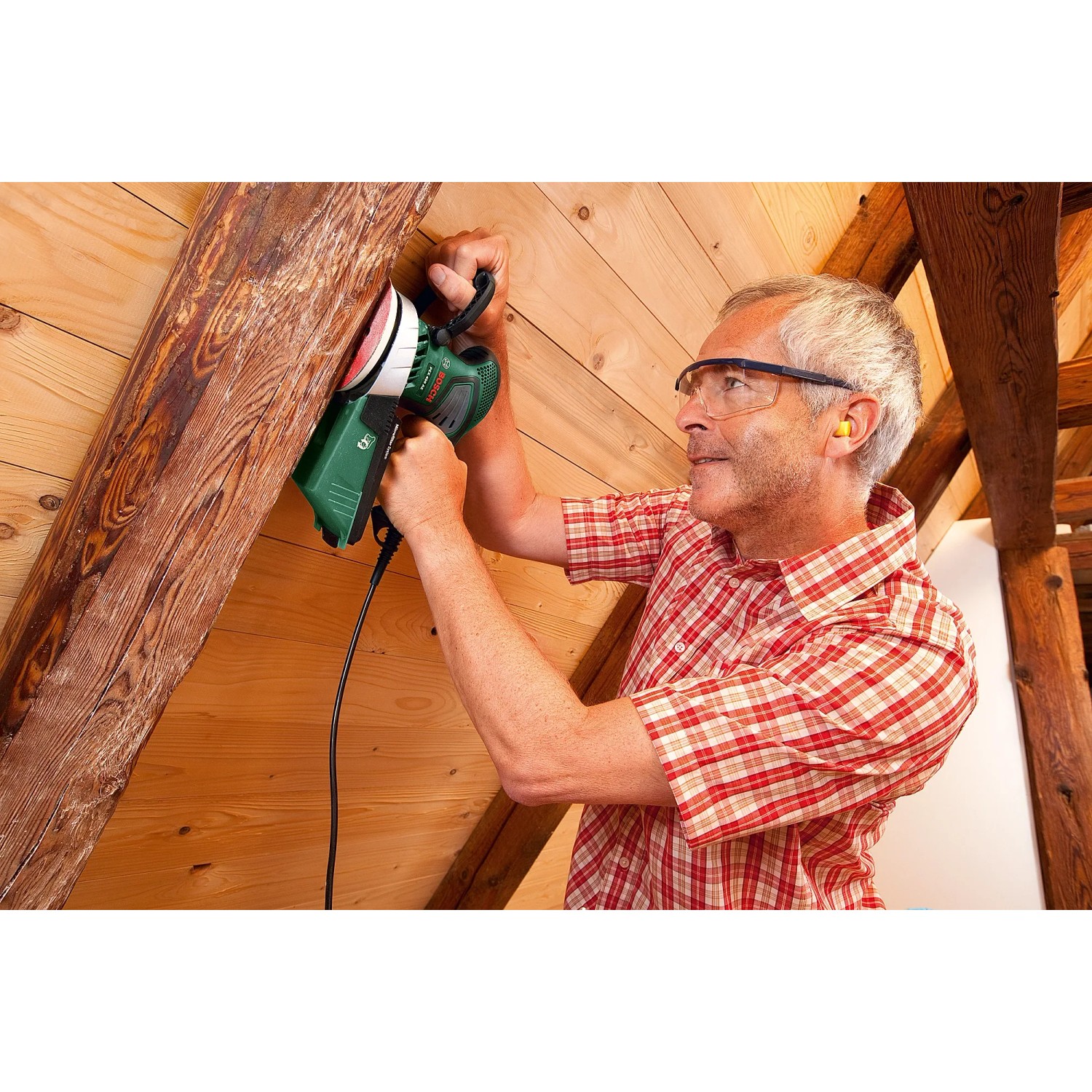 Mann schleift Holzbalken mit Bosch Exzenterschleifer PEX 400 AE. Schleifmaschine mit Micro-Filtersystem.