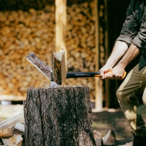 Mann spaltet Holz mit Fiskars Spaltaxt X24. Axt mit schwarzem Stiel und orangefarbenem Griff.