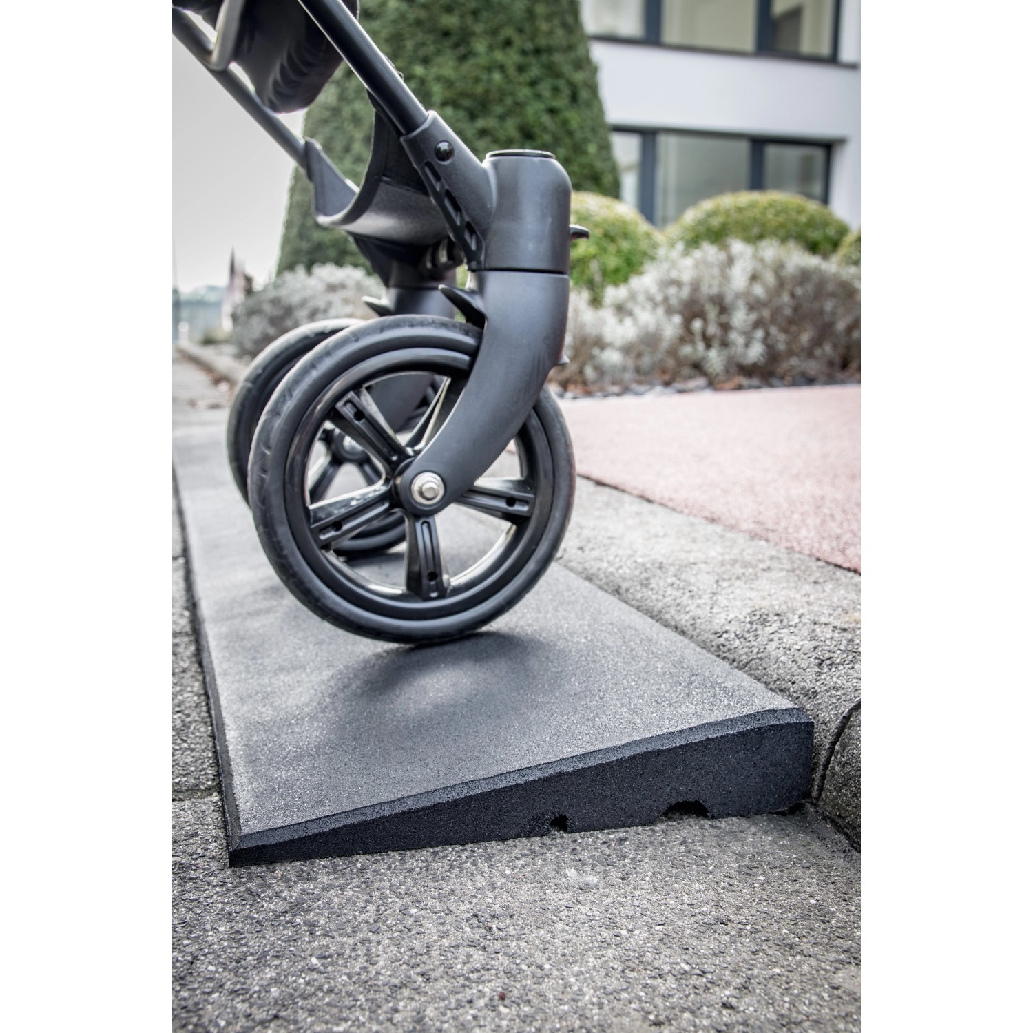 Schwarze Bordsteinrampe aus Gummigranulat mit Kinderwagenrad für leichten Zugang.