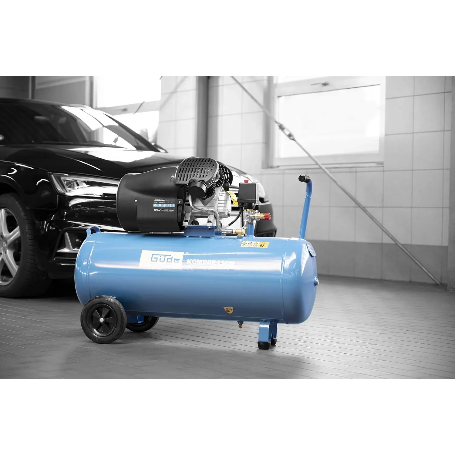 Blauer Güde Kompressor 412/8/100 mit 2 Zylindern und Transportgriff vor Auto.