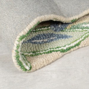 Nahaufnahme eines gerollten Flair Rugs Wollteppichs Bryony mit mehrfarbigem floralem Muster, geformten Kanten und Wollflor.