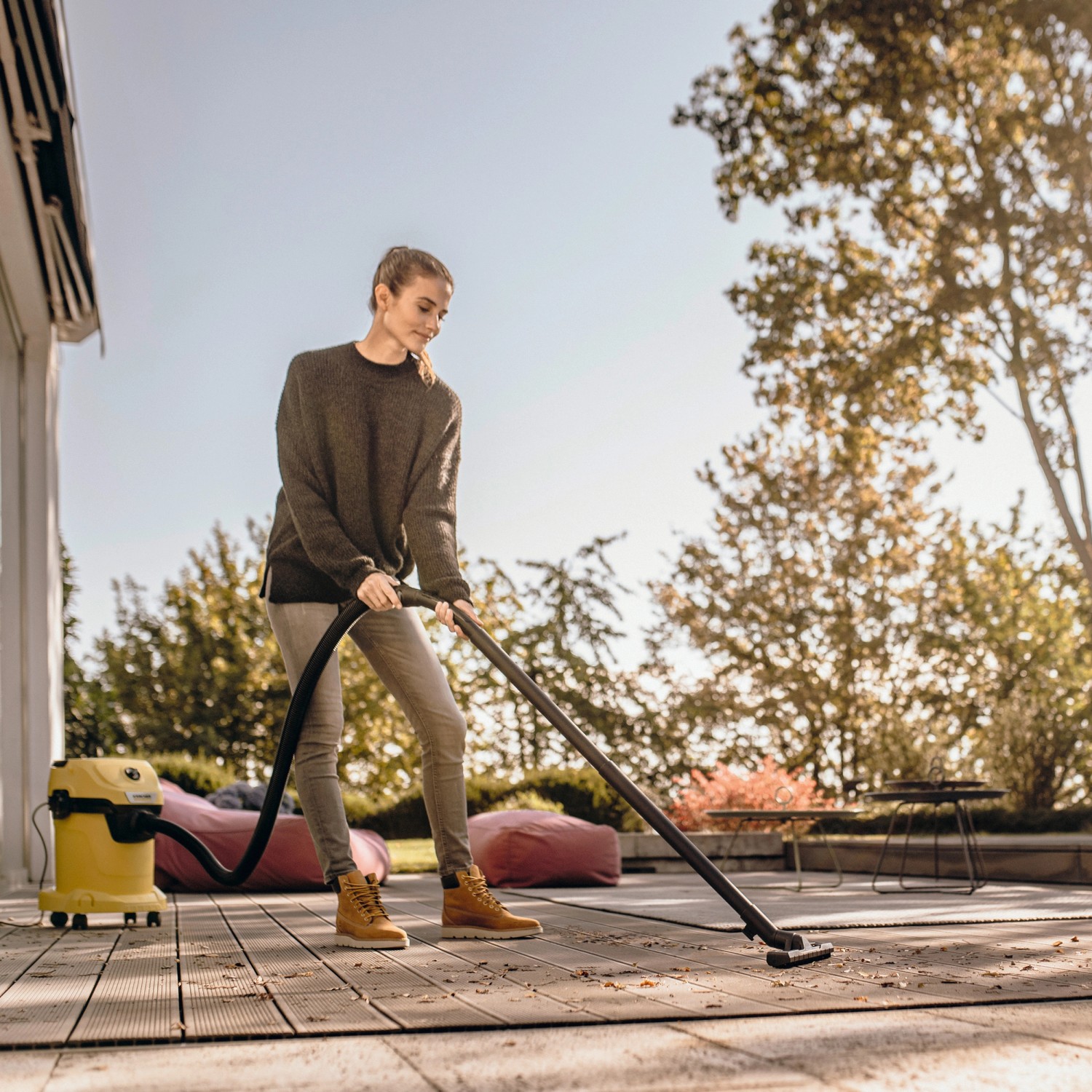 Frau saugt mit Kärcher WD 3 V-17/4/20 Nass-Trockensauger Terrasse. Gelber Sauger mit Zubehör.