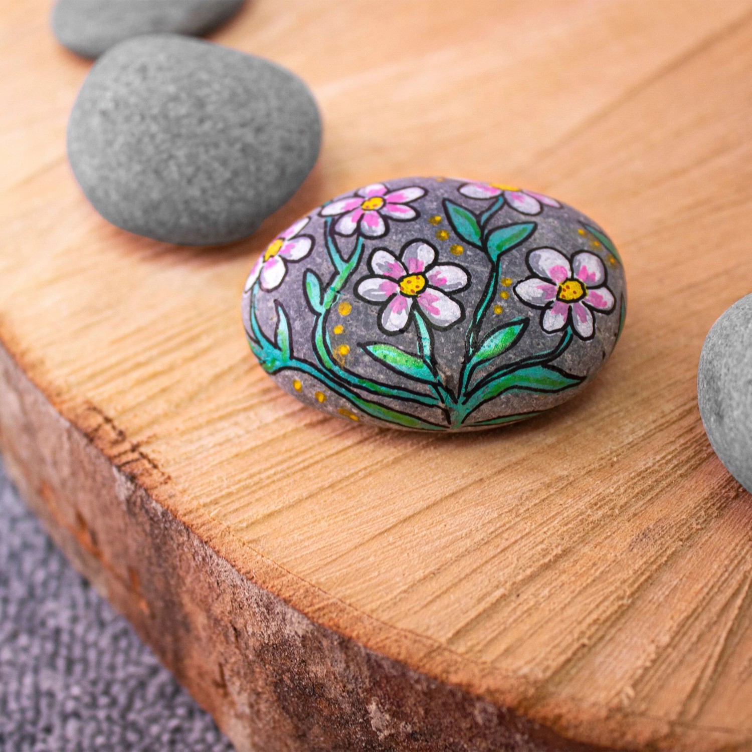Dunkelgrauer, flacher Malstein mit pink-weißen Blumen auf Holz. Ideal für kreatives Gestalten & DIY-Projekte.