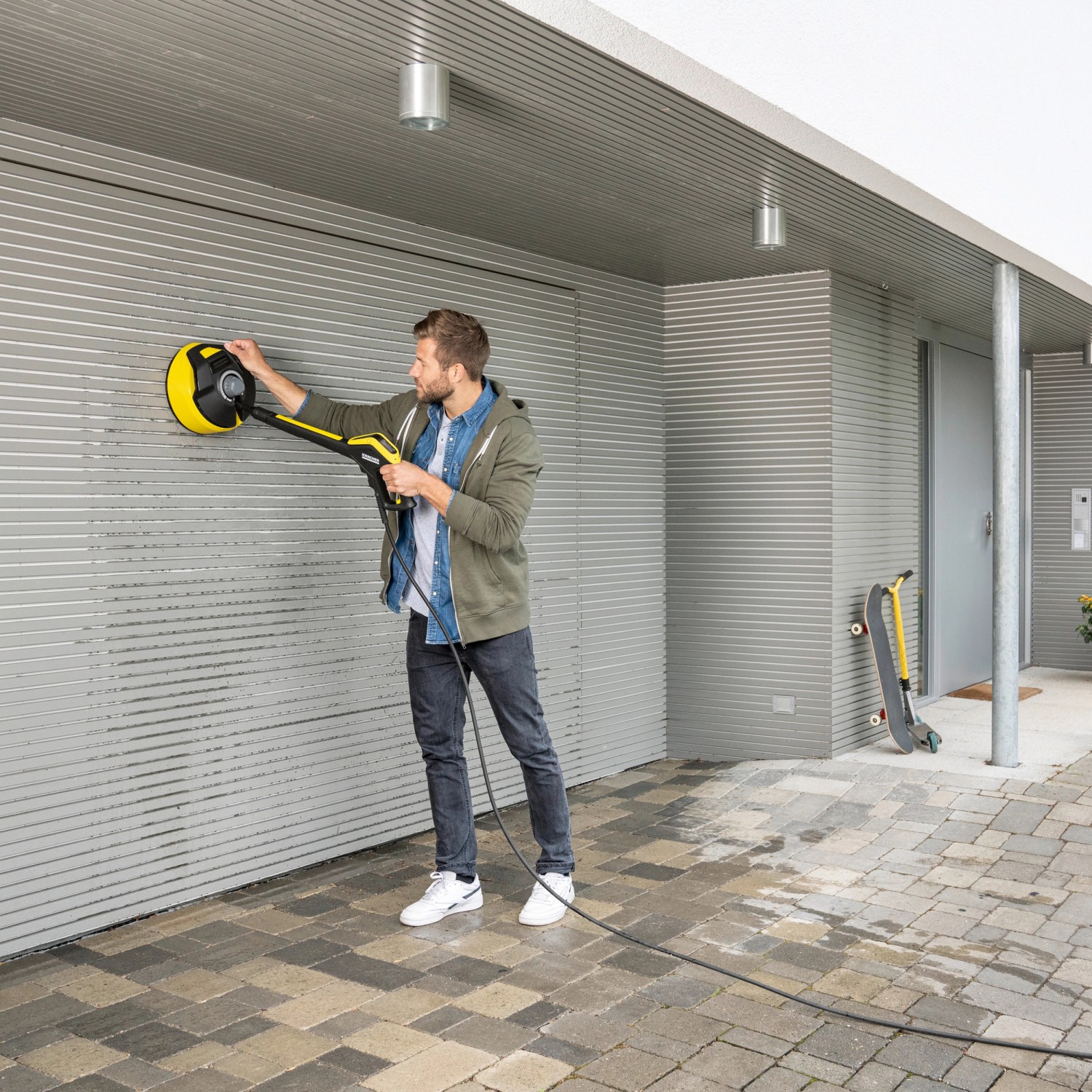 Mann reinigt Fassade mit Kärcher Flächenreiniger T 5 T-Racer. Der gelb-schwarze Bodenreiniger entfernt Schmutz.