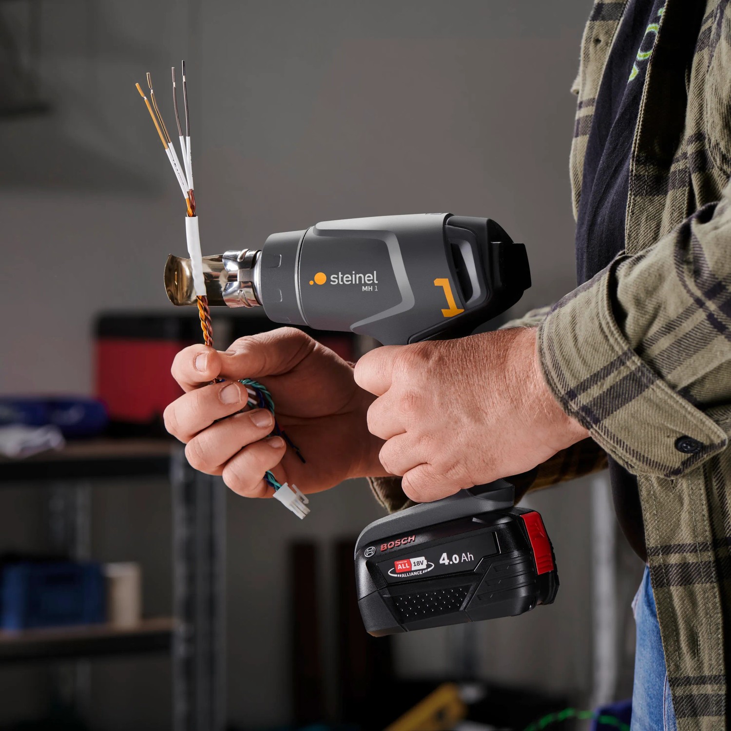 Steinel Akku-Heißluftgebläse MobileHeat 1 mit Akku und Ladegerät im Einsatz beim Schrumpfen von Kabeln.