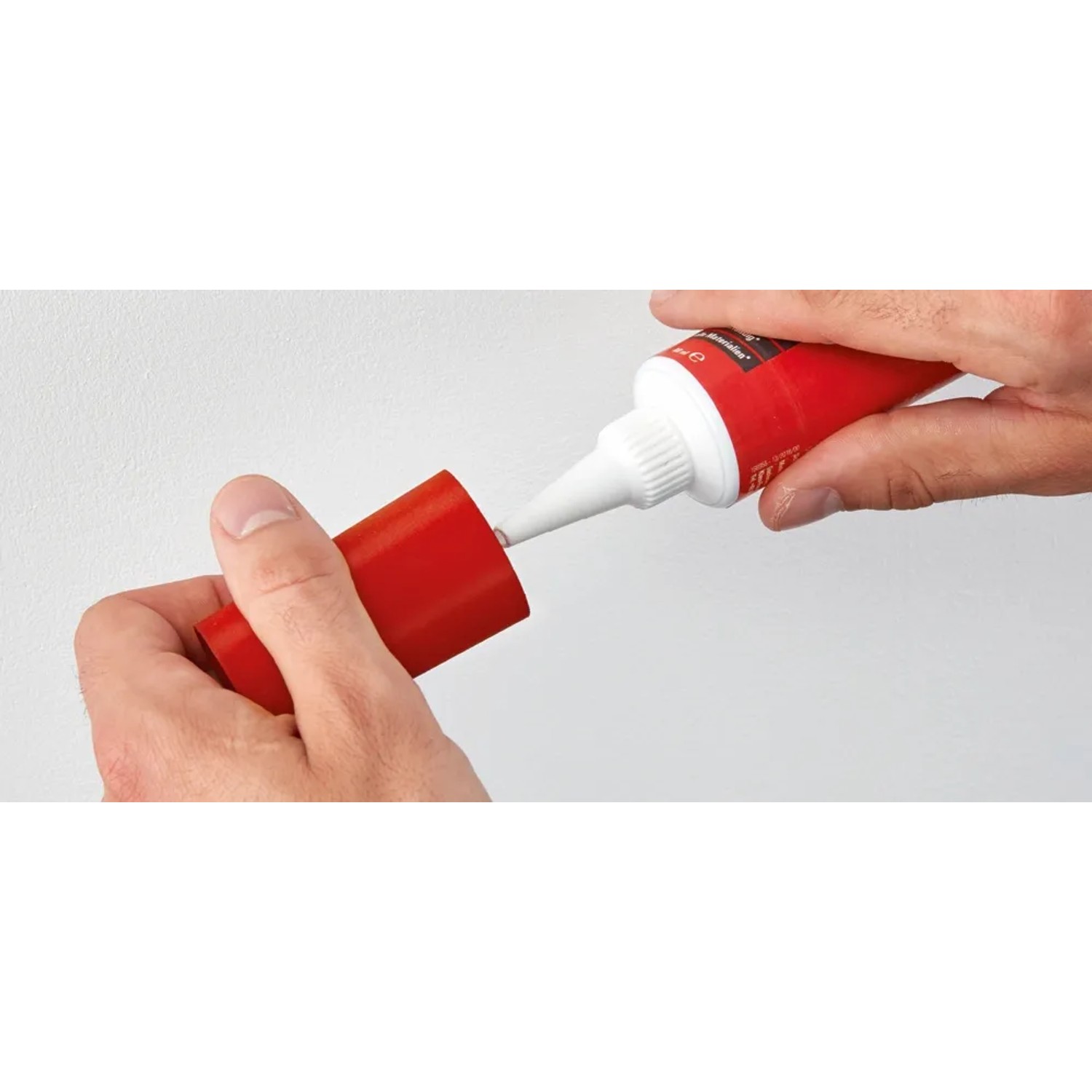 Anwendung von Fischer Dicht Kleber 80ml: Tube, Düse und roter Deckel in Händen.