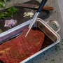Char-Broil Spitzzange hält Fleischstück in Marinade. Grillutensil für präzises Wenden.