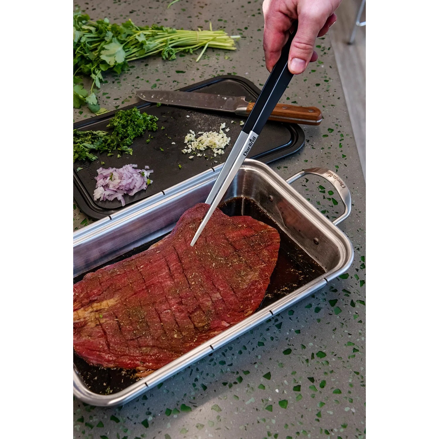 Char-Broil Spitzzange hält Fleischstück in Marinade. Grillutensil für präzises Wenden.