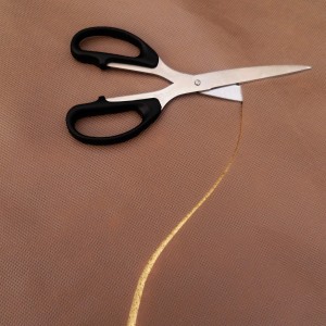 Braunen Aquagart Gartenvlies wird mit einer Schere zugeschnitten.