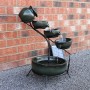 Monstershop Solar Kaskadenbrunnen Grun mit vier Schalen und Solarpanel vor einer Ziegelwand.