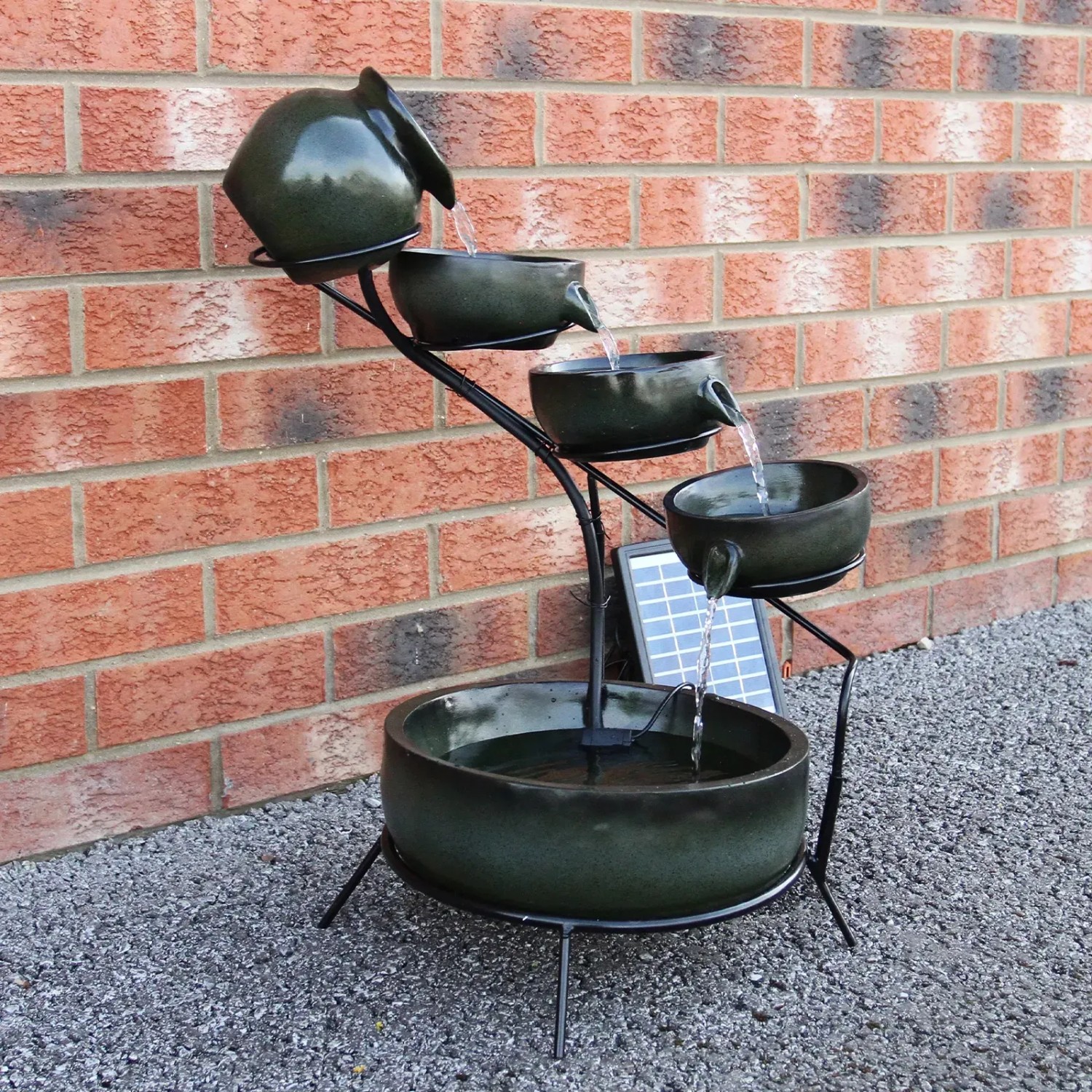 Monstershop Solar Kaskadenbrunnen Grun mit vier Schalen und Solarpanel vor einer Ziegelwand.