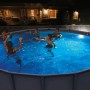 Szene mit LED Poolbeleuchtung in rundem Pool mit badenden Personen bei Nacht.