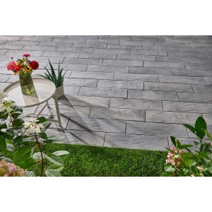 Verlegte, grau-nuancierte Nativa Dielenplatten (60x20x4 cm) als Trittsteine im Garten, mit Tisch und Blumen.