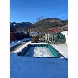 Rechteckiges Schwimmbecken mit Winterabdeckung (6x3m) im verschneiten Garten.