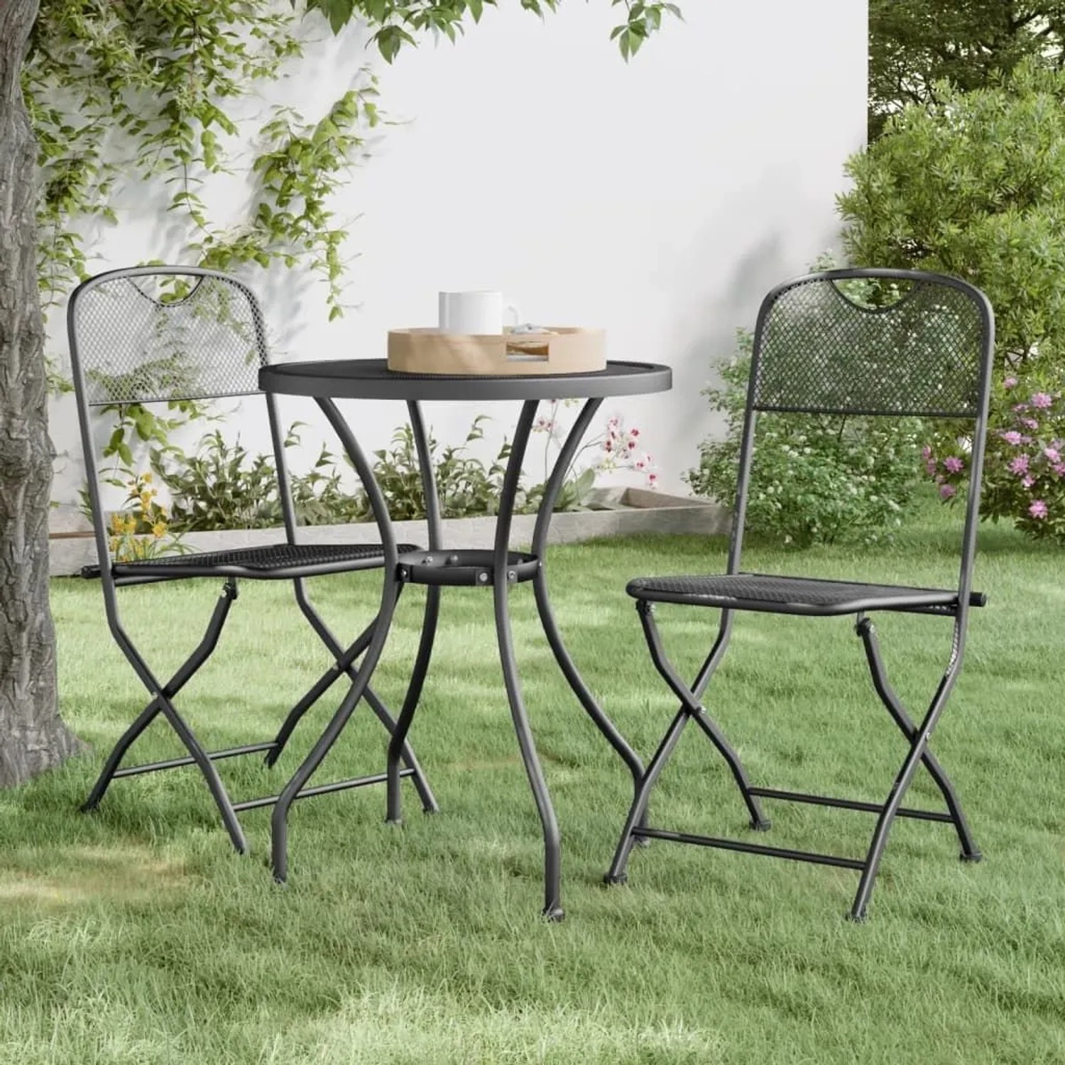 Zwei anthrazitfarbene klappbare Gartenstühle aus Streckgitter im Garten, mit einem Tisch.