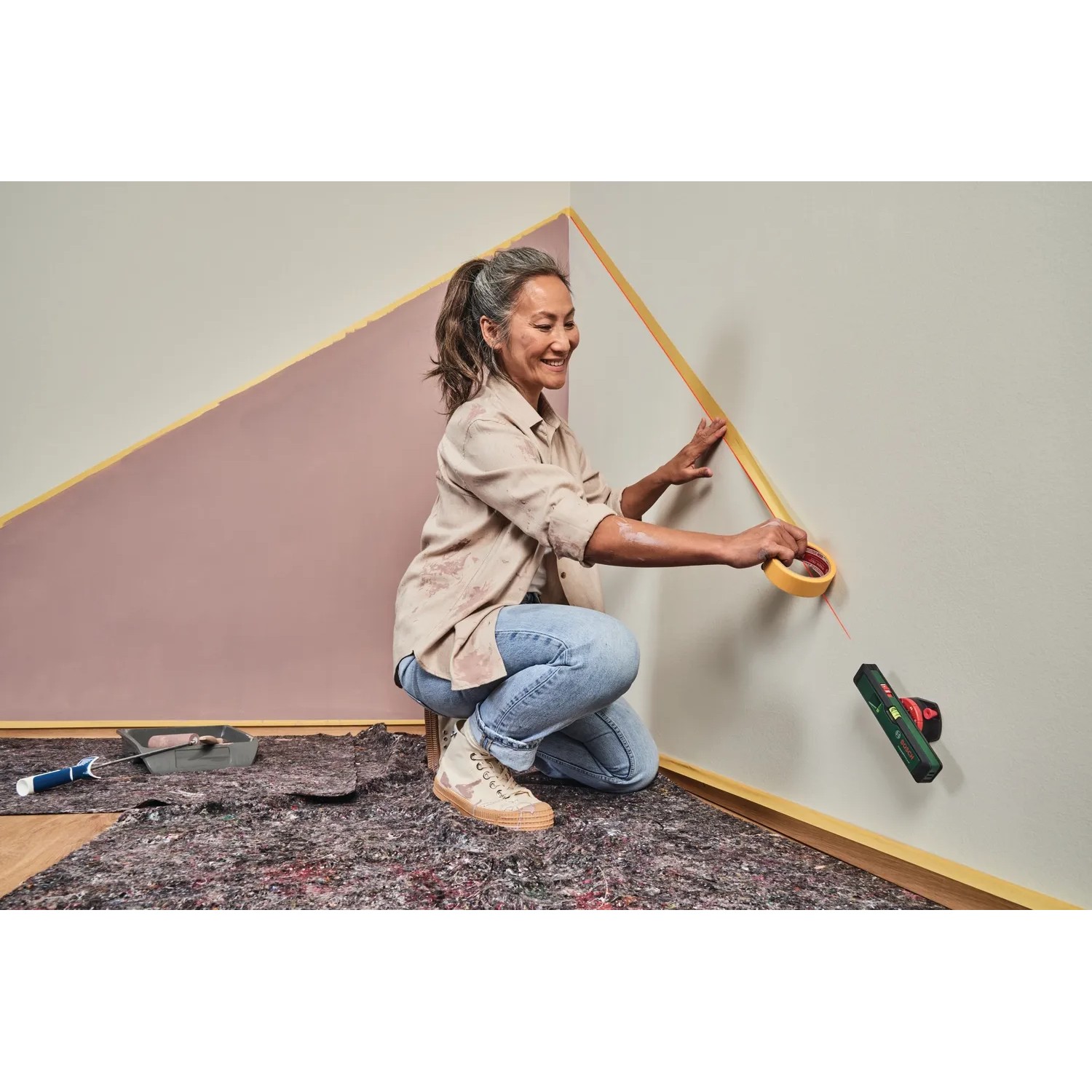Frau klebt mit Bosch Laser-Wasserwaage UniversalWallLevel eine Wand ab.