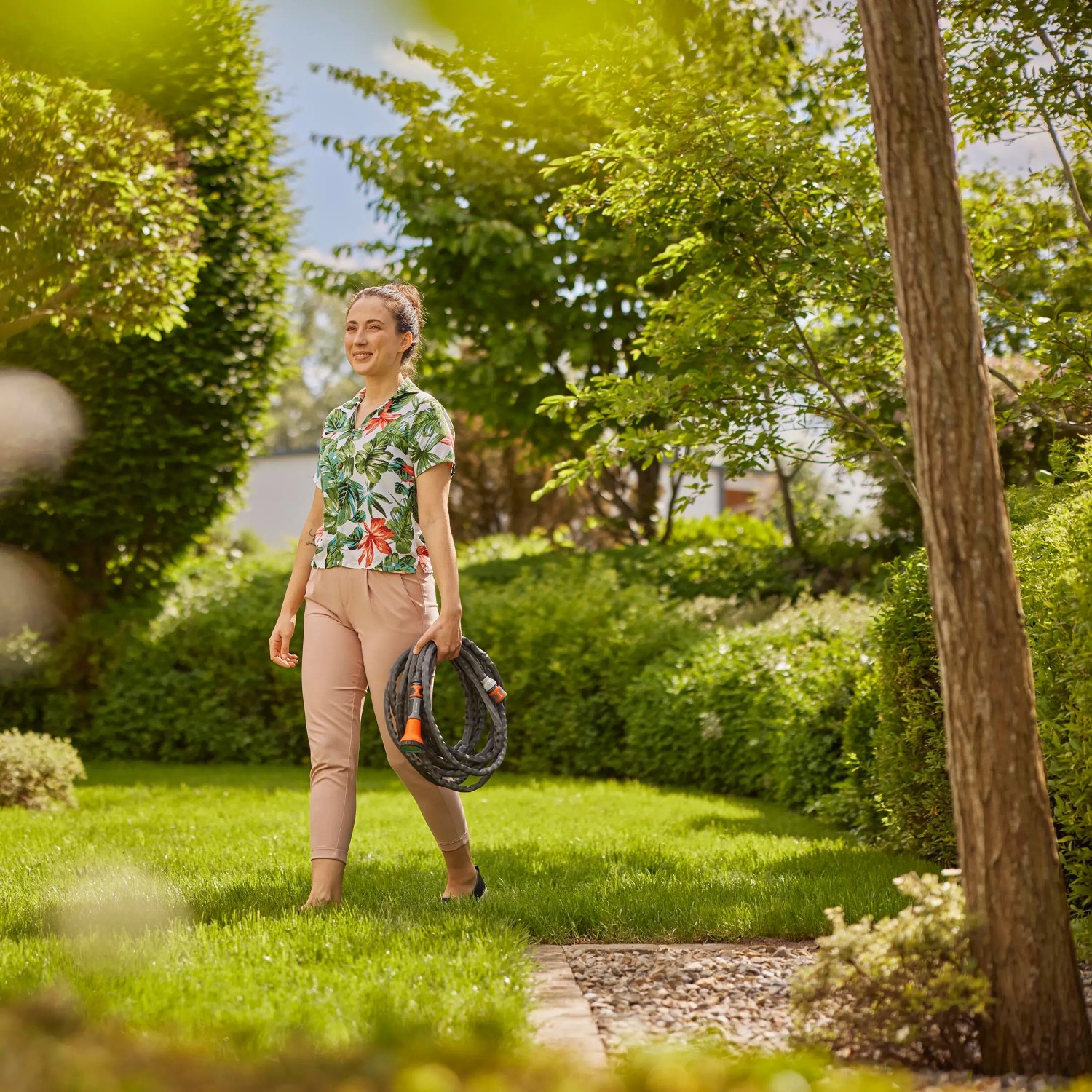 Frau trägt Gardena Gartenschlauch-Set Liano™ Life 10 m durch den Garten.