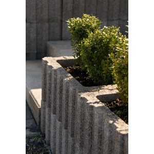 Grauer Pflanzstein (60x40x25 cm) mit Bepflanzung als Hangbefestigung.