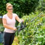 Frau schneidet Hecke mit LUX Akku-Heckenschere A-HS-20/52. Kabellose Heckenschere für präzise Gartenarbeit.