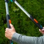Gardena TeleCut Teleskop-Heckenschere in Aktion vor grüner Hecke. Hand-Heckenschere mit ausziehbaren Griffen.