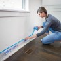 Frau bringt ScotchBlue Malerabdeckfolie mit Klebeband an Wand an.