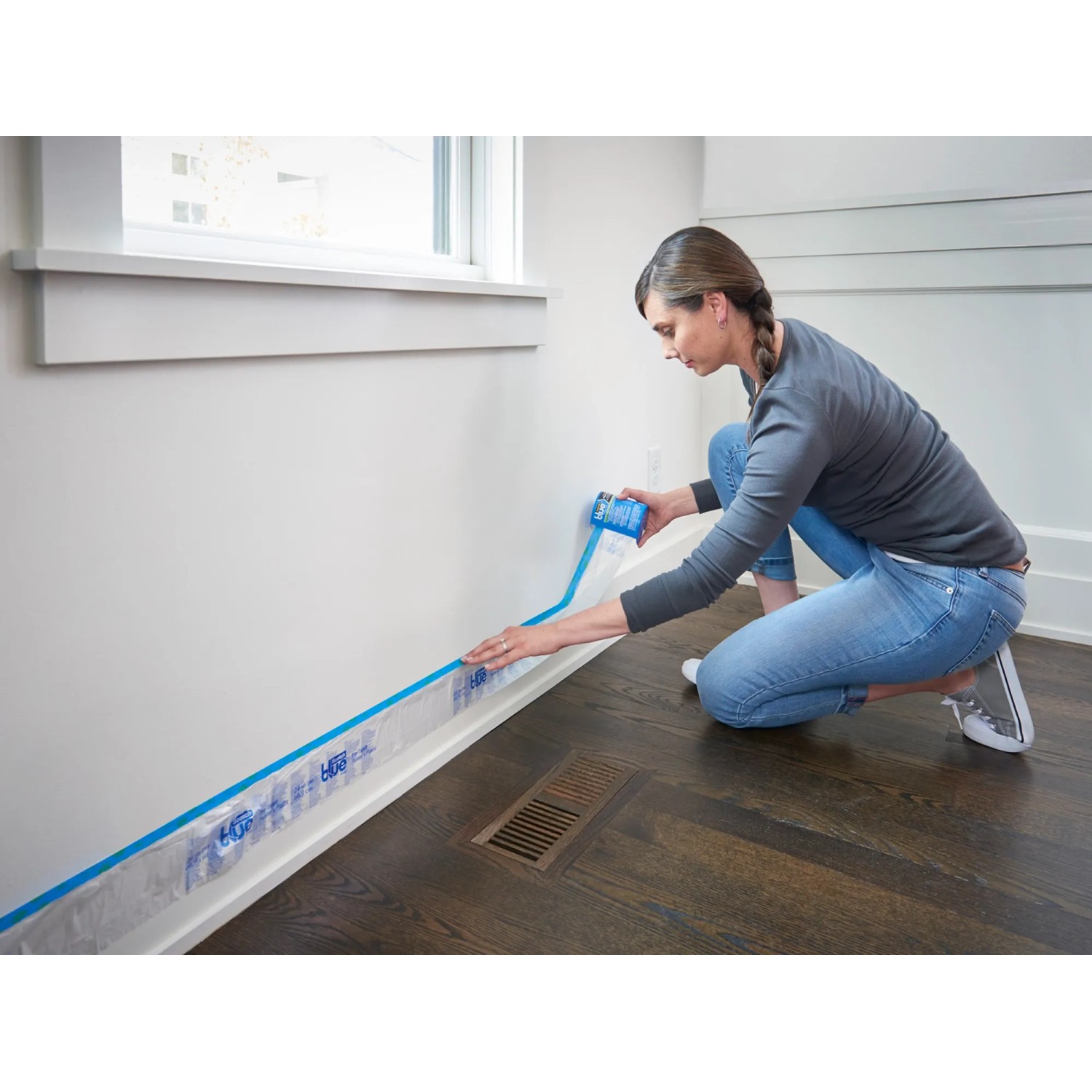 Frau bringt ScotchBlue Malerabdeckfolie mit Klebeband an Wand an.