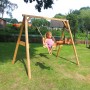 Braune Axi Doppelschaukel aus Holz mit Mädchen auf dem Schaukelsitz im Garten.