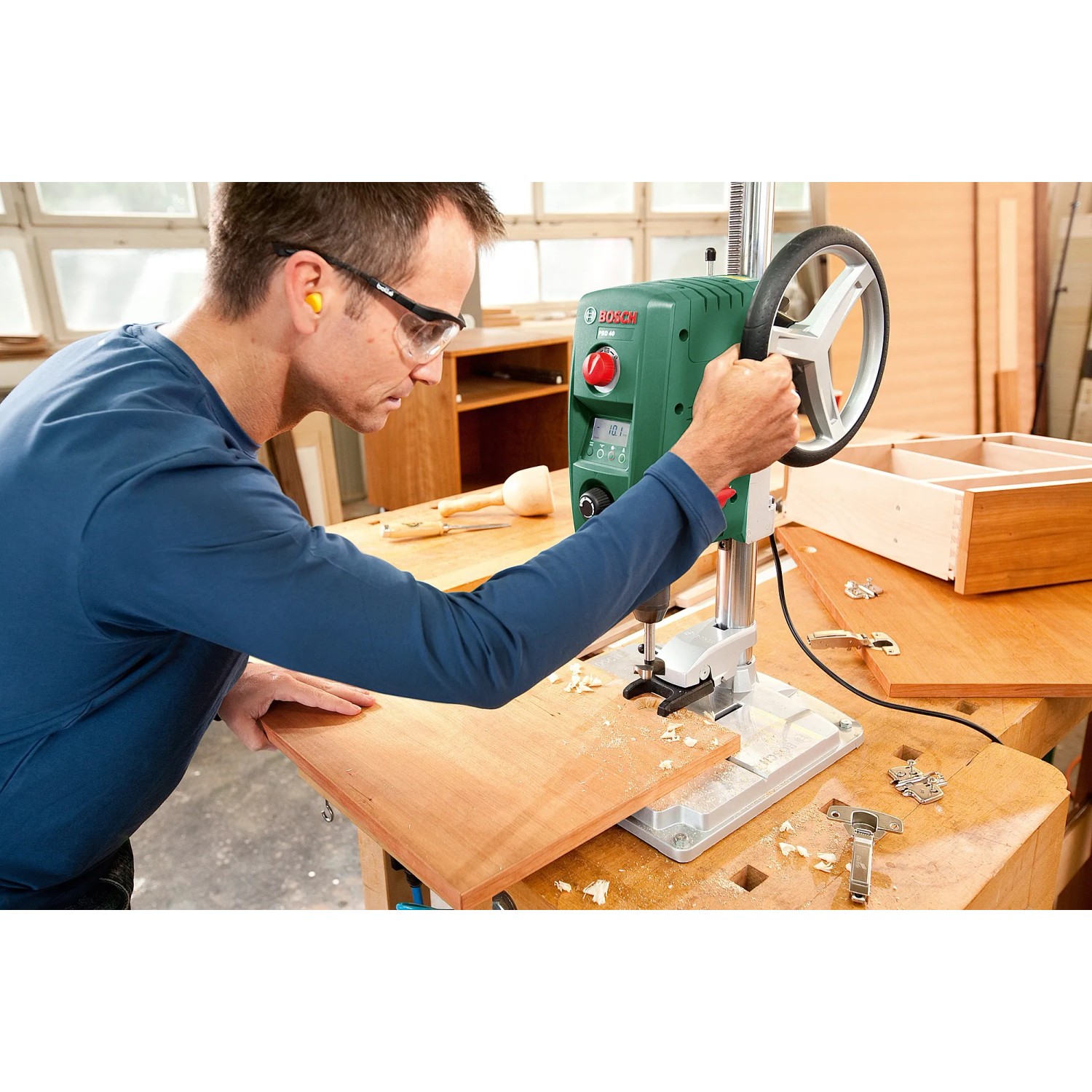 Mann bohrt mit Bosch PBD 40 Tischbohrmaschine ein Holzbrett. Präzises Bohren mit Laser.