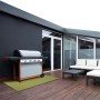 Wetterfester, grüner Outdoor Teppich Aversa 60x350 cm von KARAT auf einer Terrasse mit Grill und Sitzgruppe.
