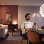 Philips Hue White Ambiance E27 LED Lampe im Wohnraum mit Nutzer, der die Lichtsteuerung per App bedient.