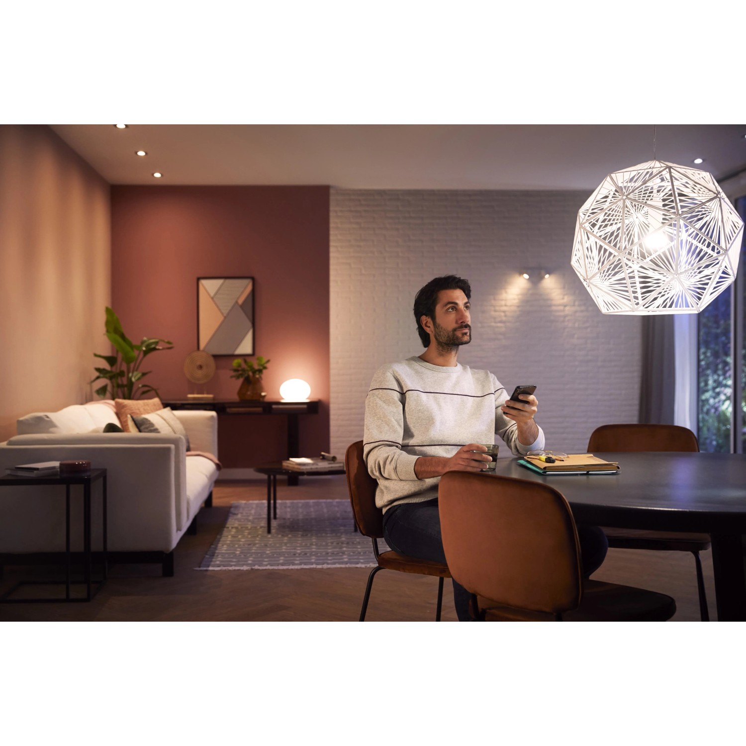 Philips Hue White Ambiance E27 LED Lampe im Wohnraum mit Nutzer, der die Lichtsteuerung per App bedient.
