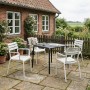 Vier weiße DELUKE LARS Kunststoff Gartenstühle auf Terrasse mit dunklem Tisch vor Ziegelhaus. Stapelbare Loungestühle.