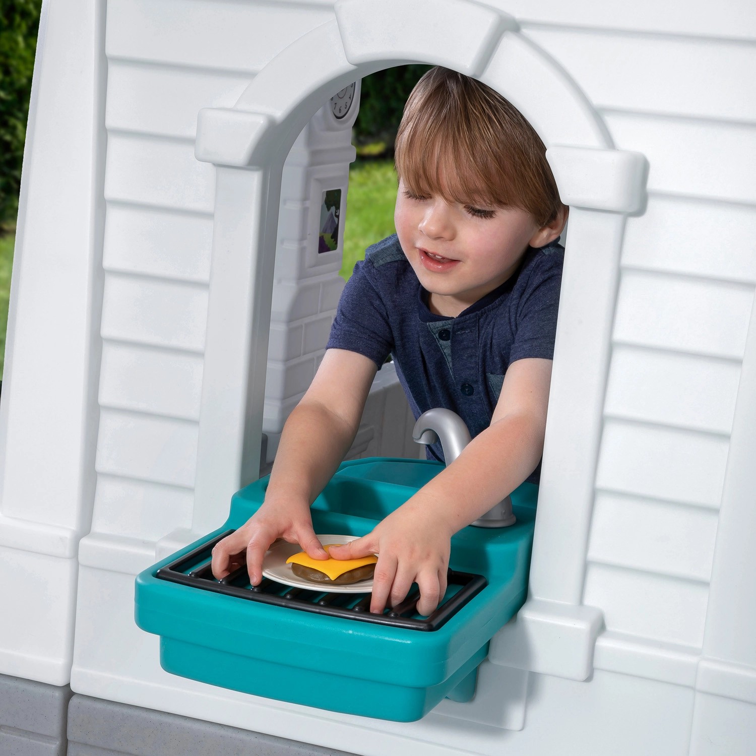 Junge spielt im Step2 Spielhaus Neat & Tidy Cottage mit Grill und Spüle.