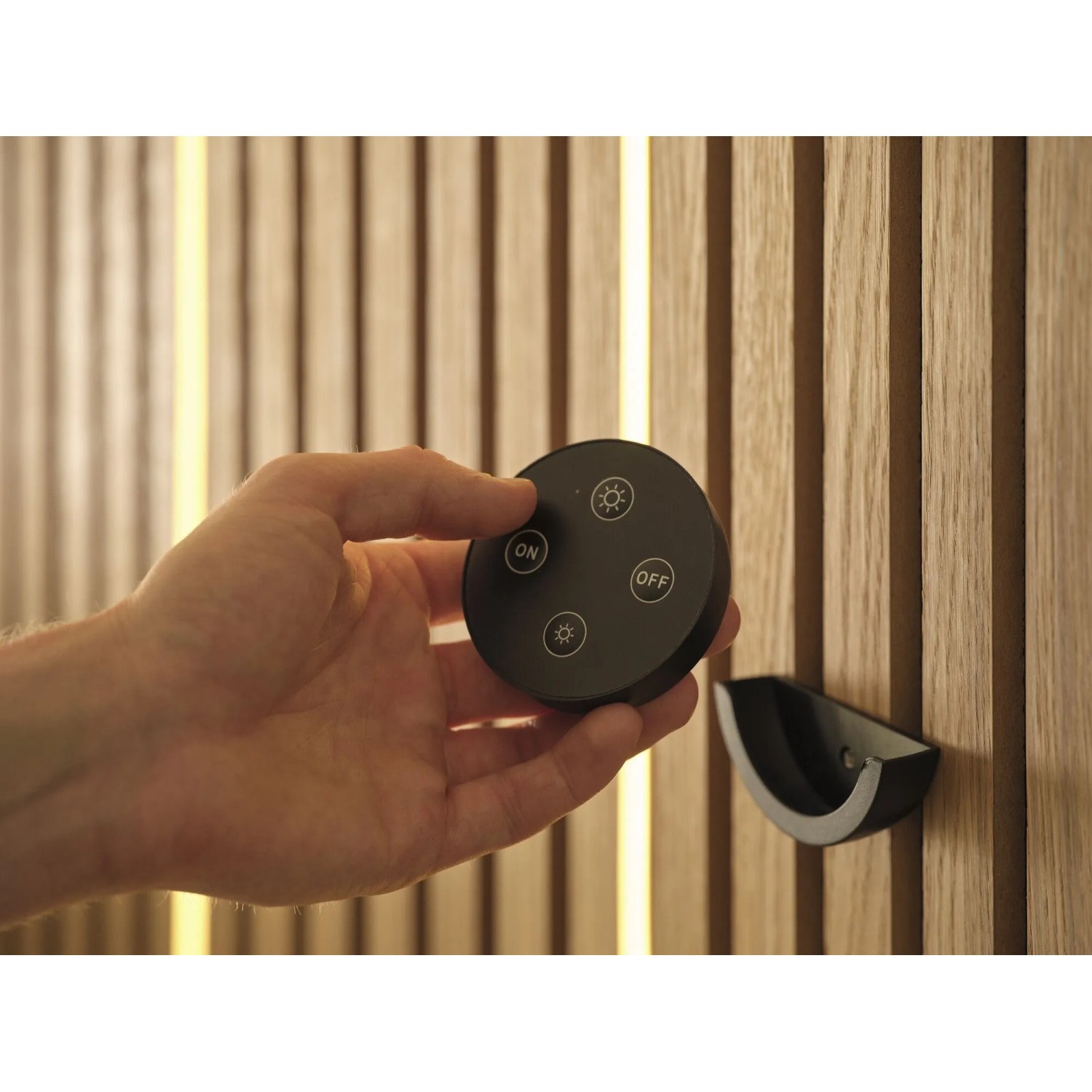 Hand hält schwarze Fernbedienung für dimmbaren OSRAM LED Streifen, warmweiß leuchtend in Akustikpaneele.