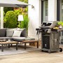 Gartenlounge mit grauer Eckcouch, Tisch und Grill auf einer Holzterrasse.
