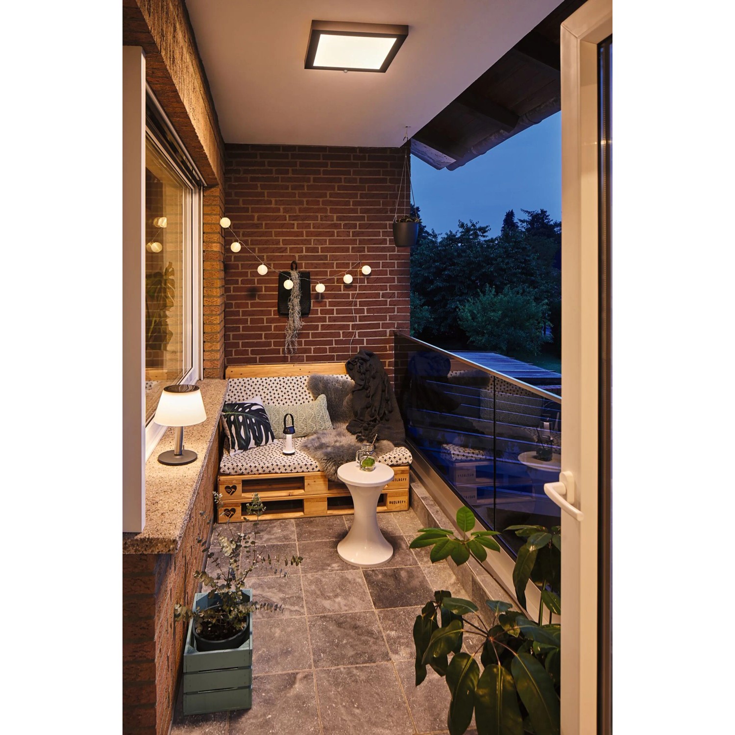 Stimmungsbild: Solar Tischleuchte Lillesol auf Balkon mit Palettenmöbeln und Dekoration.