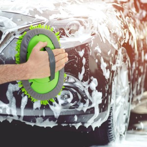 Hand wäscht dunkles Auto mit hellgrünem Mikrofaser Autowaschhandschuh. Effizientes Autozubehör für gründliche Reinigung.