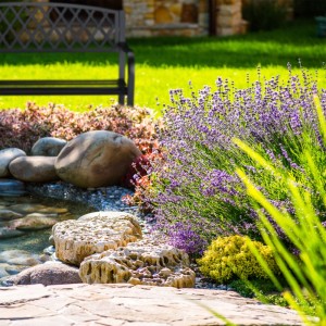 Schwarze Relaxdays Gartenbank aus Gusseisen und Stahl mit Flechtmuster für 2 Personen, platziert in einem grünen Garten.