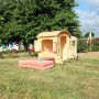 Naturfarbenes Kinderspielhaus Patty mit Runddach im Garten, 133x108x145 cm.
