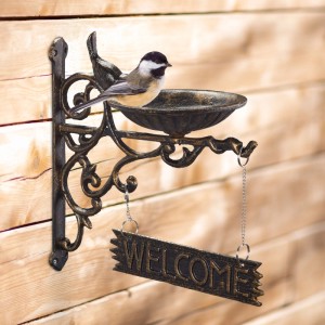 Bronzene Gusseisen Vogeltränke mit Welcome Schild für Wandmontage. Ein kleiner Vogel sitzt auf der Schale.