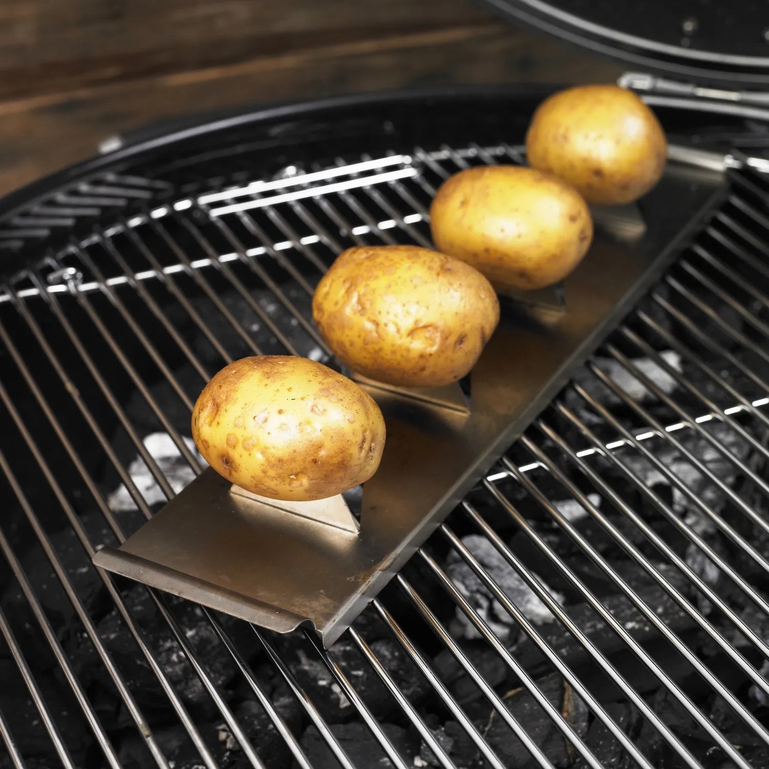 Rösle Kartoffelhalter aus Edelstahl mit vier Kartoffeln auf einem Grill.